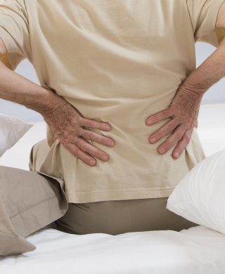 Man sitting in bed with pillows at his right and left side clutching his lower back, used to explain getting an MRI for back pain