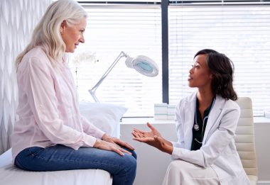Mature woman in consultation with female doctor sitting on examination table, used to explain dense breast tissue