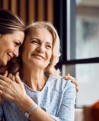 A photograph of two women holding each other close and smiling while looking off-camera, used to explain how family history of breast cancer impacts risk